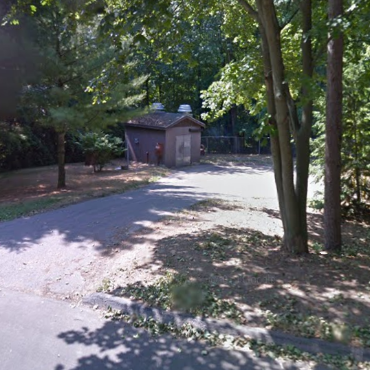 Small sewer lift station building off a street in a heavily wooded area.