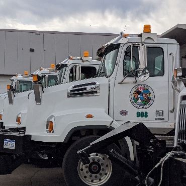 White snow plows lined up next to each other, with part of building in the background