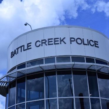 Circular building corner, white tiles along the top, windows underneath. Says Battle Creek Police. 