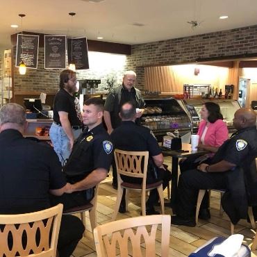 About a dozen people, including police officers, sitting at or standing near café tables. 