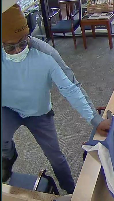 Thin black man in dark pants, light blue long sleeve shirt, brown Carhartt hat, with glasses.