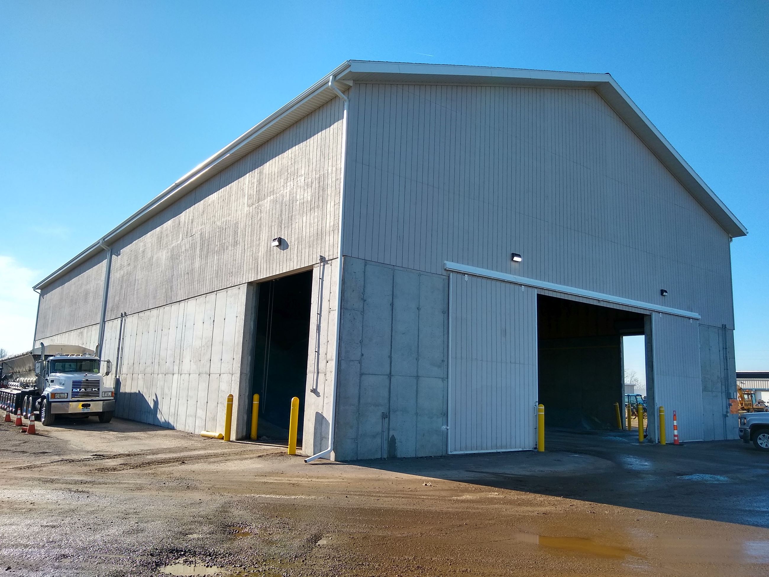 Large pole barn type building against blue sky, concrete drive around it, semi truck next to it