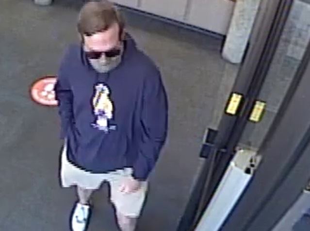 White man with brown hair wearing dark blue hoodie, khaki shorts, face mask, sunglasses